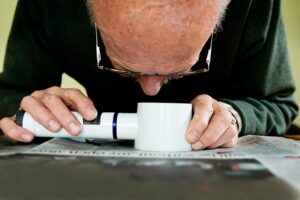 Senior man holding an illuminated magnifying glass he uses to help him read because he suffers from Wet Macular Degeneration
